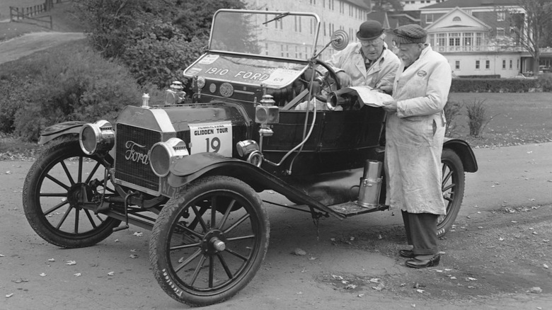 Black and white photo of a Model T Ford. Two men in white coats are discussing a document.