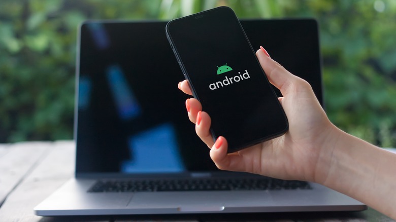 person holding phone with Android in front of MacBook