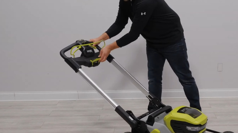 Man changing Ryobi push mower handle height using handle release lever