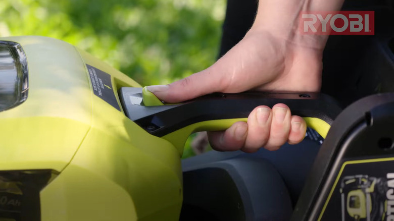 Hand pushing the height adjustment key on Ryobi push mower