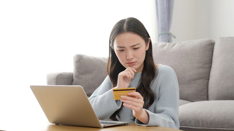 woman looking at credit card with laptop open 