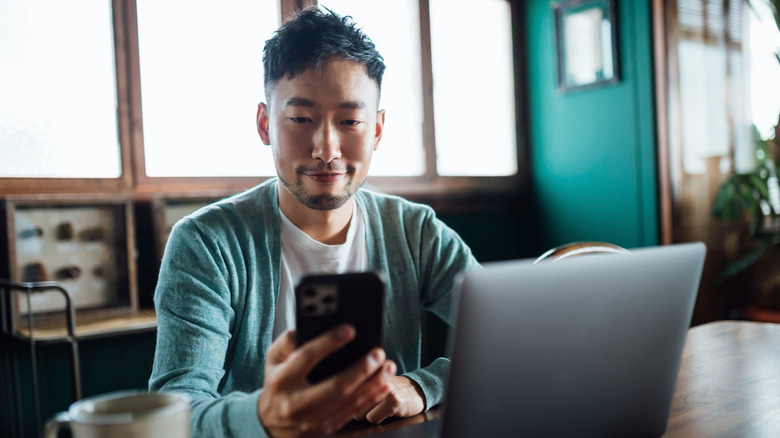 man using iphone and laptop