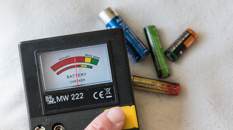 Hand holding battery tester with four batteries in the background