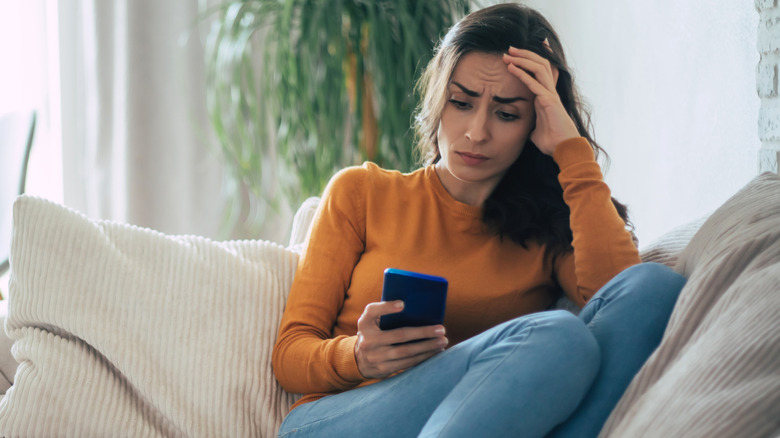 sad woman on couch using smartphone