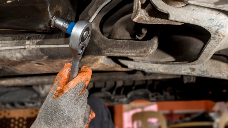 A person using a ratchet and socket to remove an oil drain plug