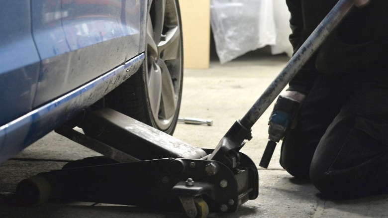 A person using a floor jack to lift a car off the ground