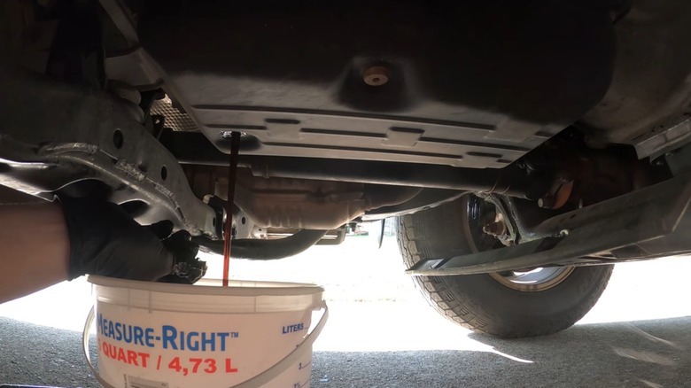 A person draining the fluid from their transmission into a clear container