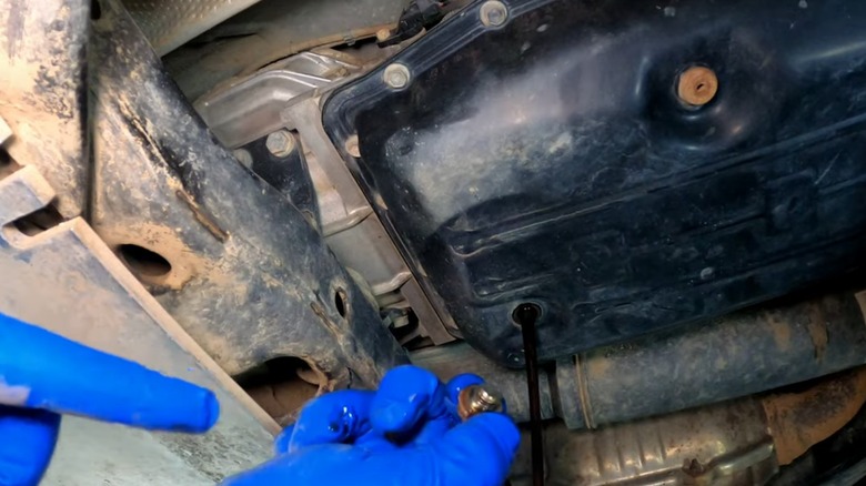 A person removing the drain plug from their transmission fluid pan