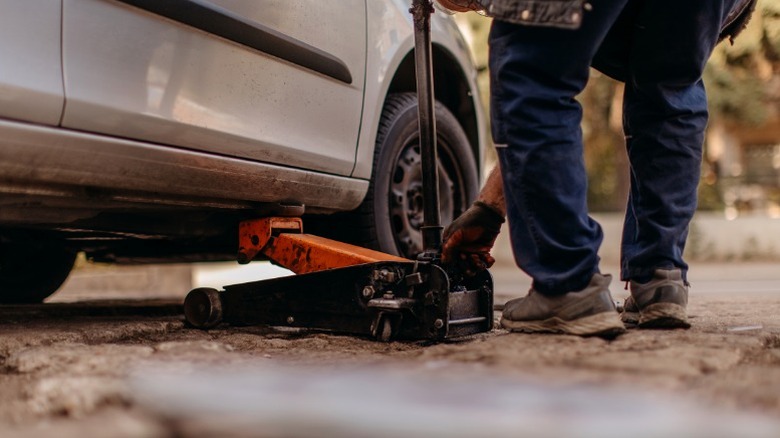 A person using a floor jack to lift their car off the ground