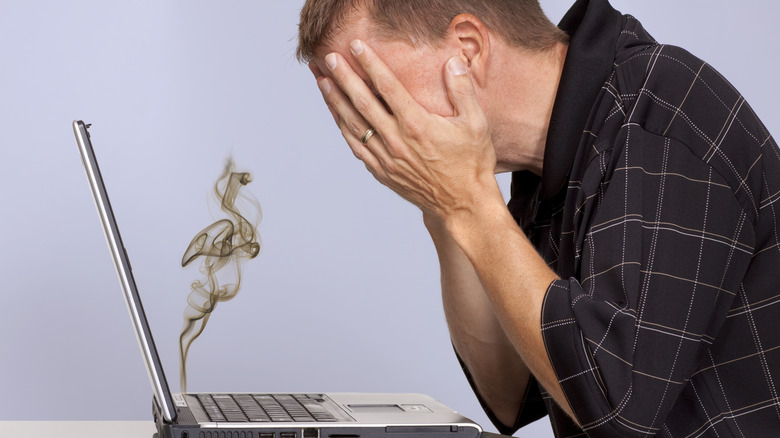 A man hides his face in despair as his laptop is burning up