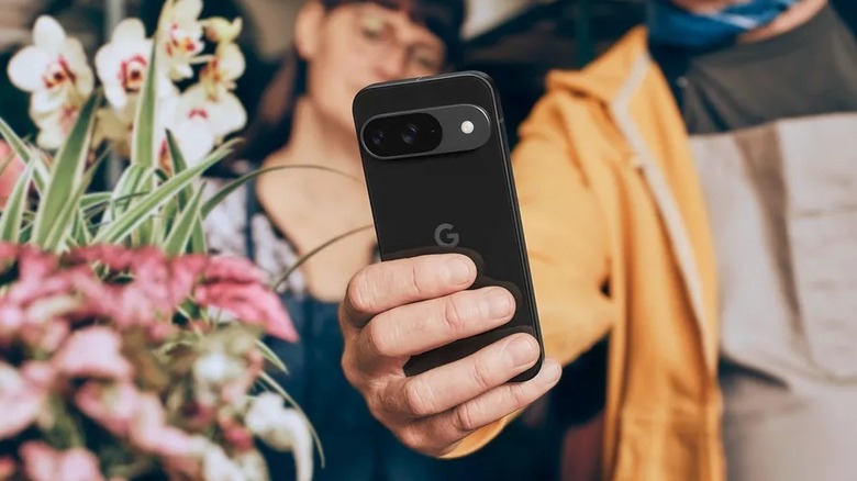 Man holding black Google Pixel 9 next to a bunch of flowers