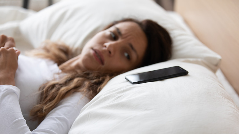 Woman looking at smartphone on pillow