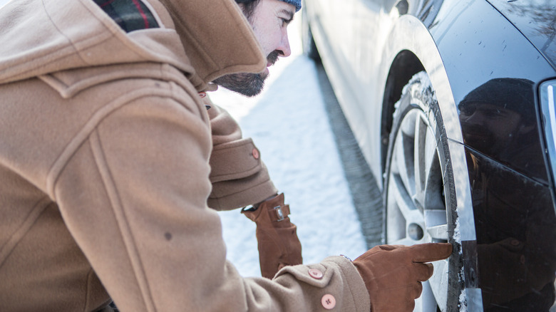 Man checking car tires in snow