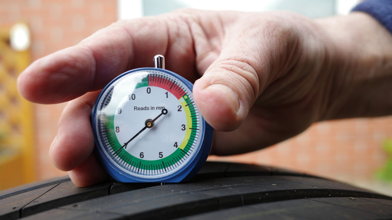 Hand using dial tire tread depth gauge on tire