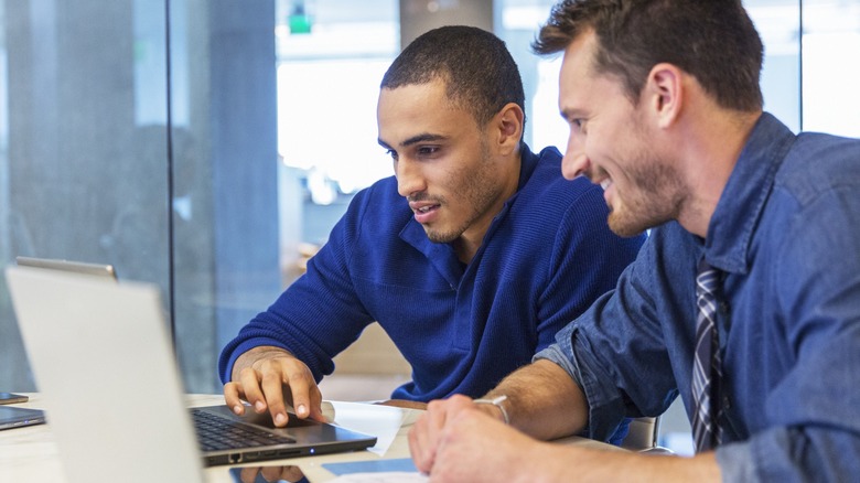 Two men checking their laptops.