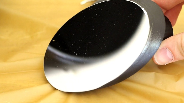 A dusty telescope mirror held by two fingers on a gold-colored tablecloth.