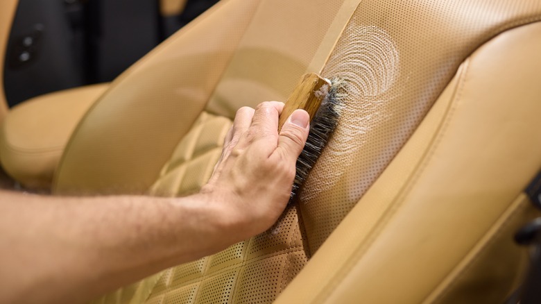 Hand holding a brush cleaning a brown perforated leather car seat