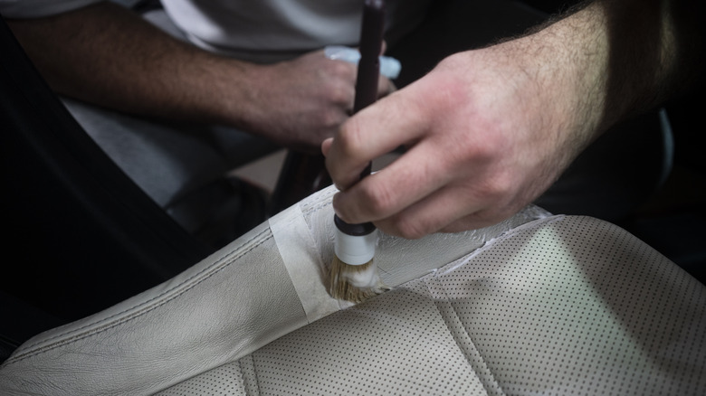 Hand holding a detailing brush cleaning a beige perforated leather car seat