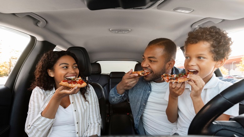 A father, daughter, and son eating pizza inside a car