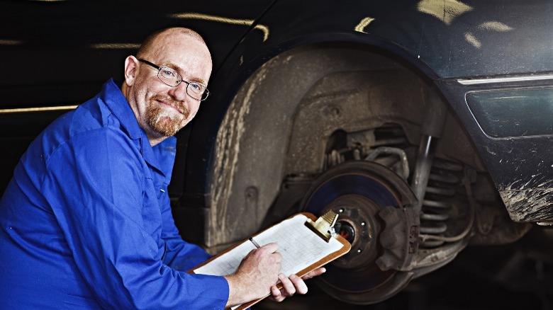 A man smiling next to a car's exposed wheel well