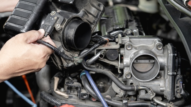 an image of a person removing the air intake tubing/filter housing from the front of an engine throttle body