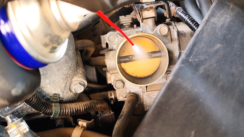 a person spraying throttle body cleaner into their engine throttle body