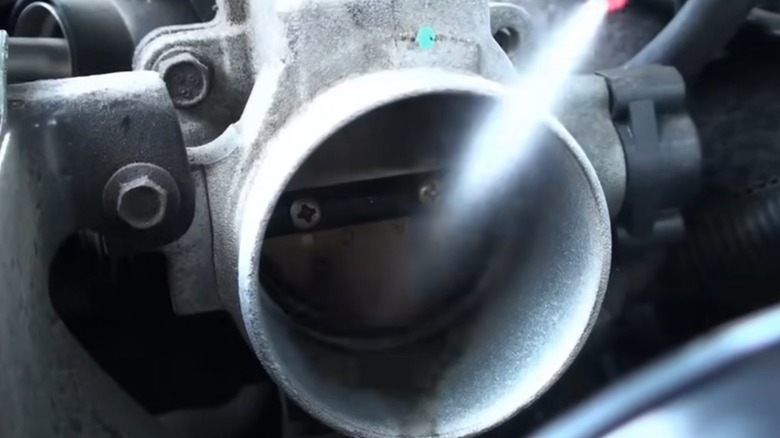 a closeup image of someone spraying throttle body cleaner into an engine throttle body