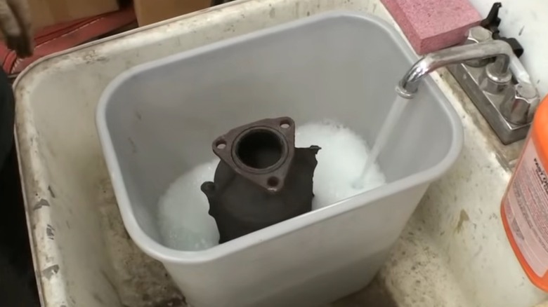 A catalytic converter sitting in a bucket of soapy water while a faucet fills the bucket