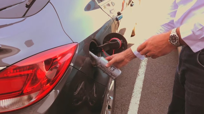 A person pouring a catalytic converter cleaner into their fuel tank