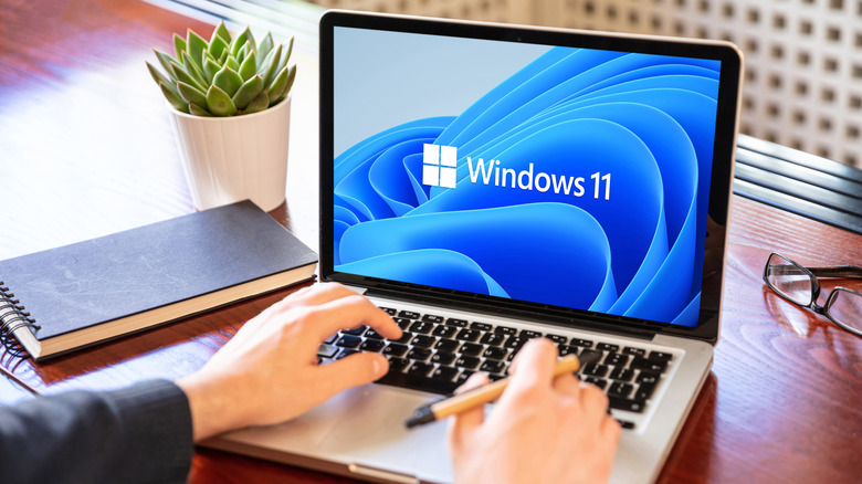 Person typing on laptop keyboard with Windows 11 logo on screen