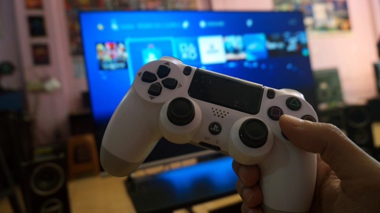 person holding white ps4 controller in front of screen