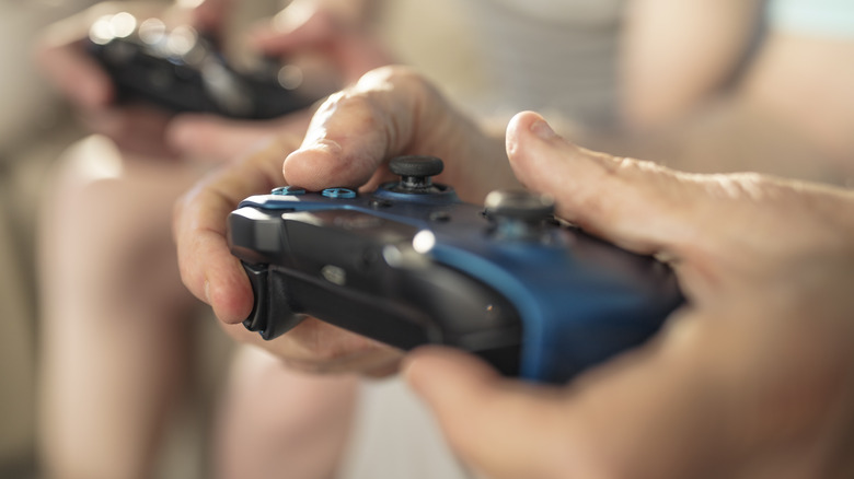 Close up of two people playing on blue Xbox controllers