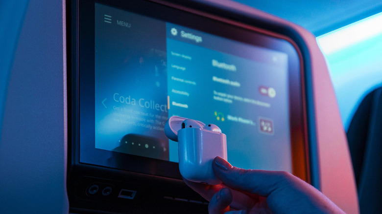 In-flight entertainment system showing Bluetooth menu with hand holding AirPods in front of screen