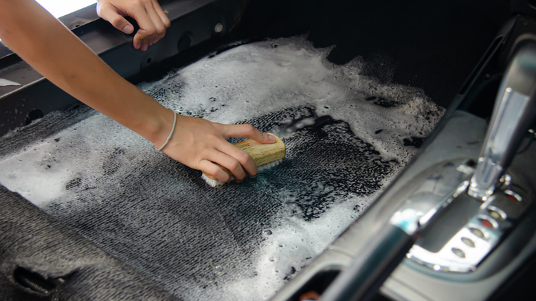 person scrubbing driver's side carpet