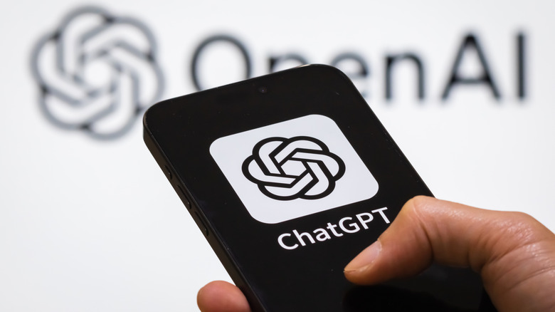 ChatGPT logo on phone in front of out of focus OpenAI logo background