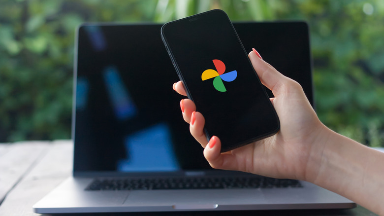 Woman holding a phone showing Google Photos icon with MacBook in the background