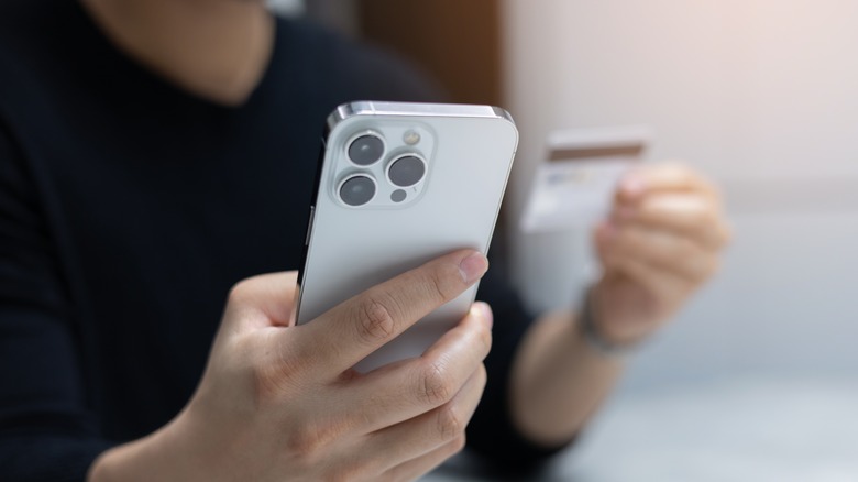 Man wearing a black t-shirt holding an iPhone and a credit card