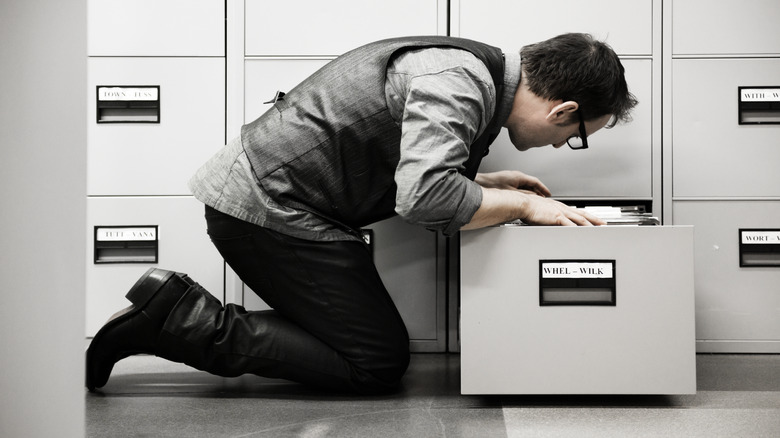 person hunched over open filing cabinet