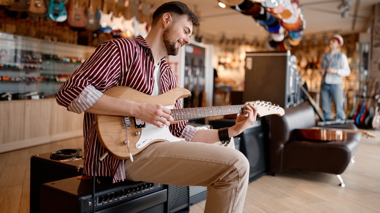 guy playing a guitar and sitting on an amp in a guitar shop