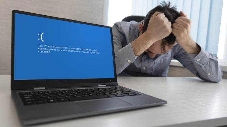 Man frustrated with laptop showing Blue Screen of Death