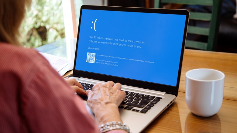 Person using laptop with blue screen error