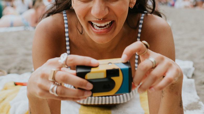 Woman smiling and holding a disposable camera on the beach