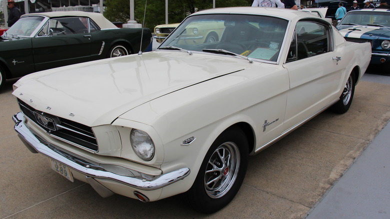 A Wimbledon White 1965 Ford Mustang K-Code Fastback parked with other Mustangs.