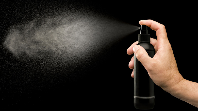 Hand holding a small black spray bottle which is spraying moisture into the air - black background