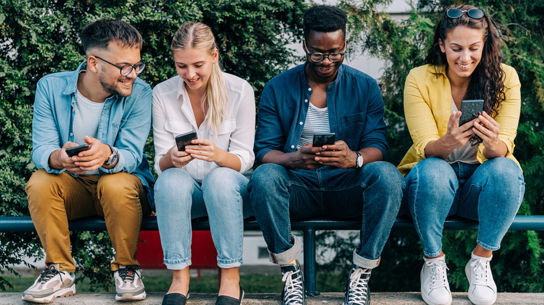 Group of people sitting together, looking at smartphones