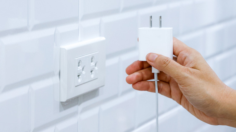 Hand holding charging brick next to wall outlet