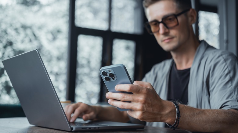 Man wearing glasses using laptop and iPhone