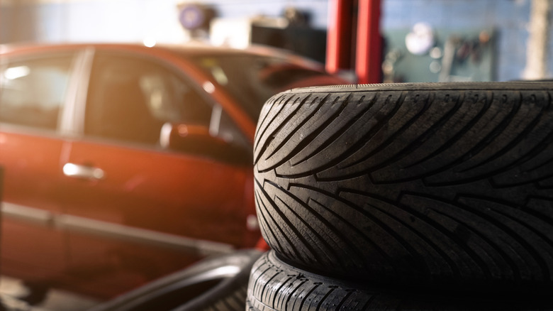 Stacked tires in auto shop with a red car in background