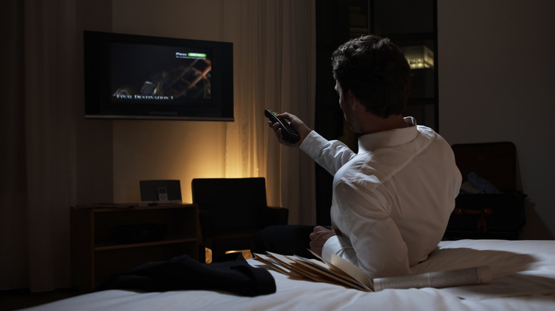 person laying on bed aiming controller at screen