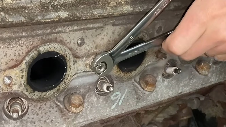 A Man Using Two Wrenches And Two Nuts To Loosen Bolt Out Of An Engine Block